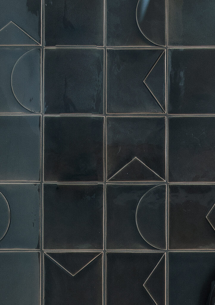 Close-up of dark charcoal Smink Studio relief tiles with raised circles, triangles and lines.