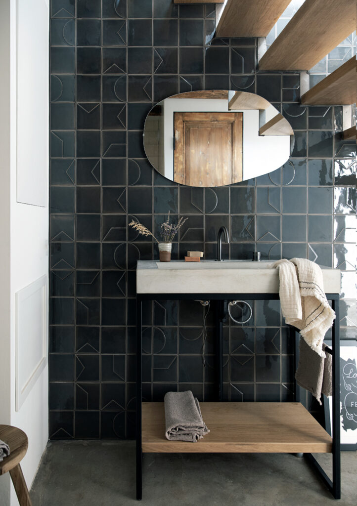 Bathroom by Natalie Visser with a concrete basin and oval mirror, walled in dark Smink Studio relief tiles with raised lines.