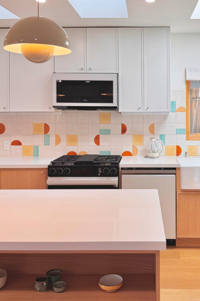 Kitchen with a white pendant lamp and a splashback of white Smink Studio handmade tiles dotted with screen-printed colour.