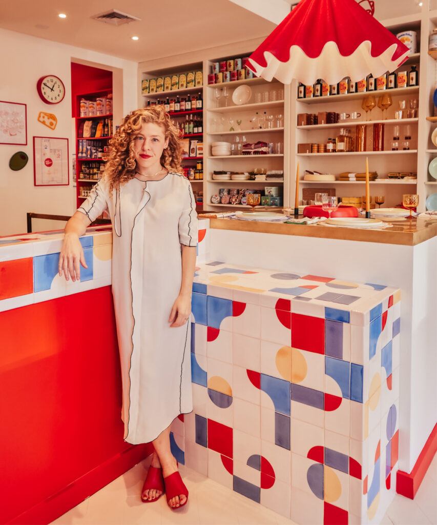 Woman beside the Big Night shop counter in New York, clad in Smink Studio handmade tiles with red, blue and yellow screen-printed shapes.