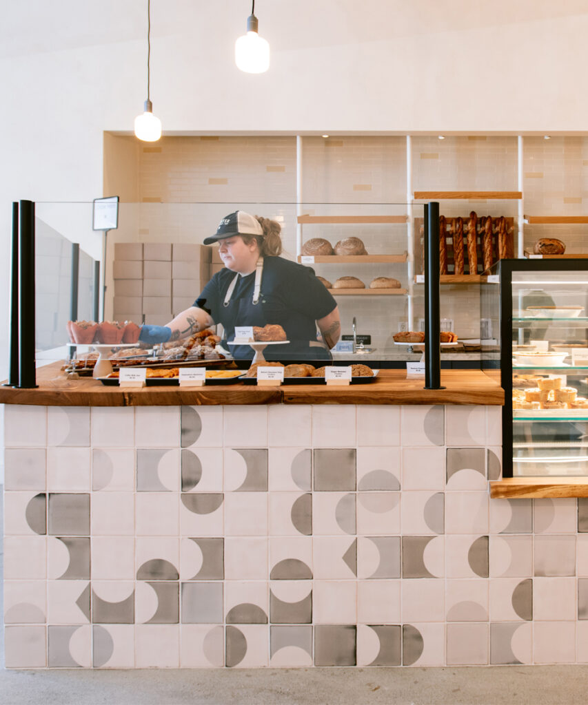 Baker behind the counter at Starter Bakery, faced with white Smink Studio tiles screen-printed with grey half-circles.