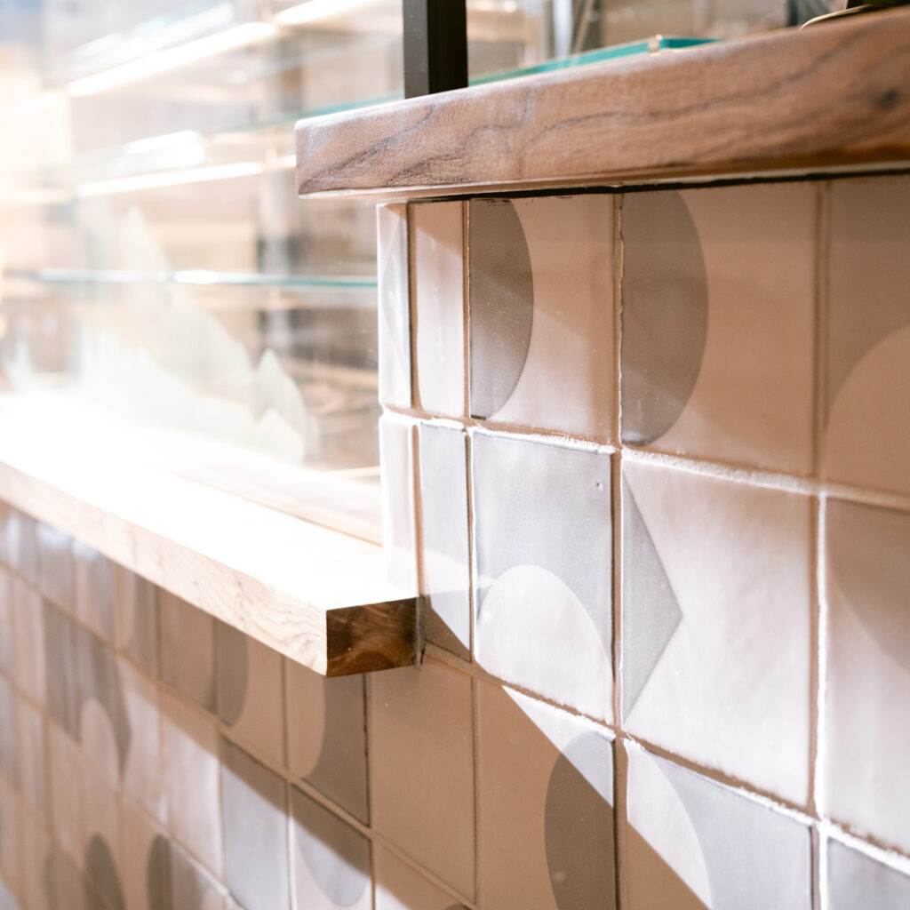 Close-up of the Starter Bakery counter in white Smink Studio glazed ceramic tiles with grey screen-printed shapes.