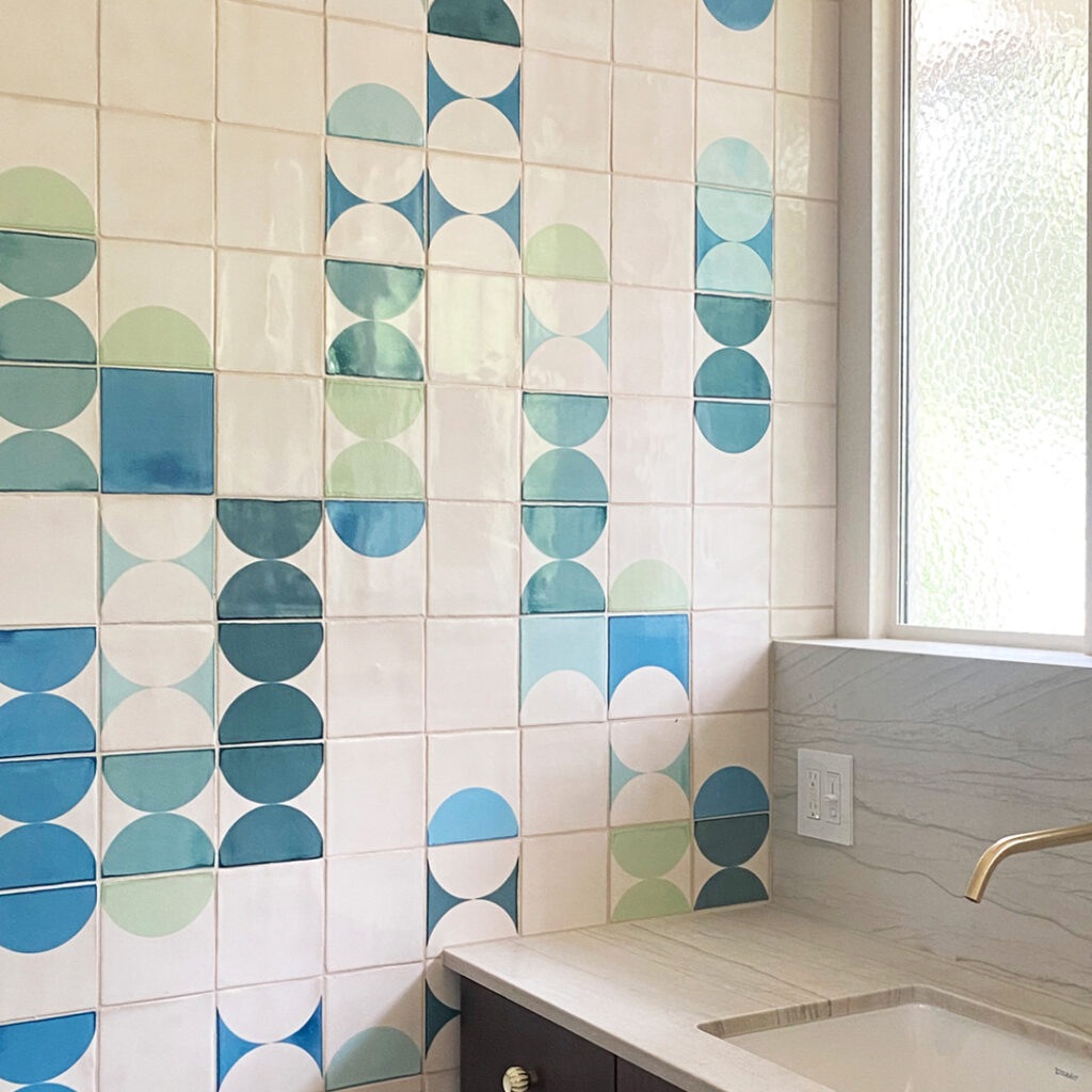 Bathroom basin by a window, walled in white Smink Studio Bubblebath handmade tiles with blue and green screen-printed half-circles.