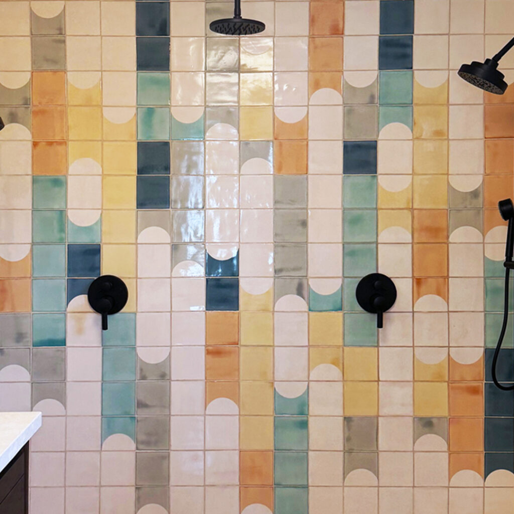 Shower wall of Smink Studio Waterfalls tiles: cream screen-printed arches over handmade tiles in teal, ochre, orange and grey.