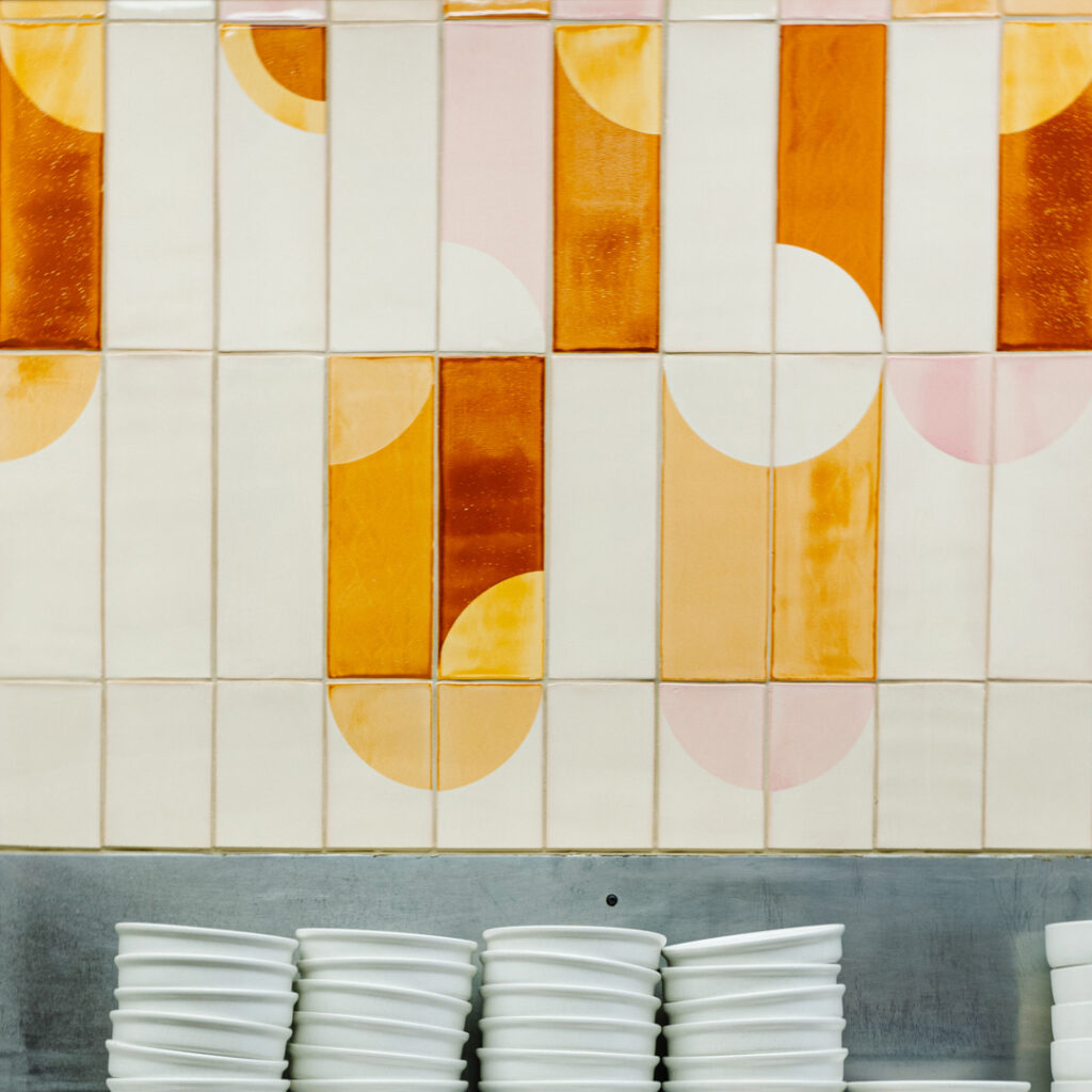 Detail of vertical Smink Studio glazed ceramic tiles at Próximo, with screen-printed half-circles in amber, orange and pink.