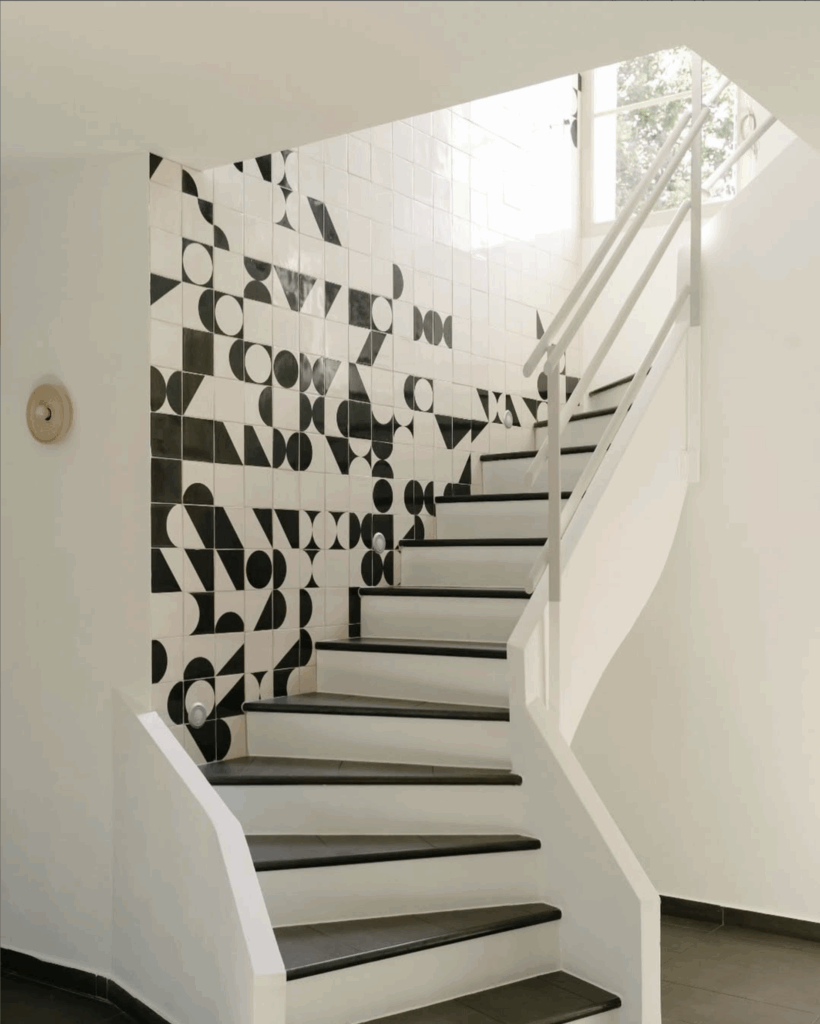 White winding staircase beside a wall of white Smink Studio handmade tiles with black screen-printed geometric shapes, for Imraum Design.