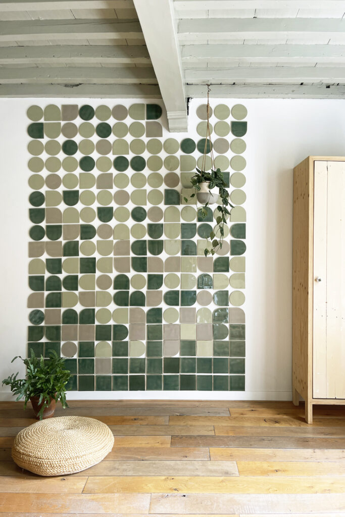 Smink Studio shaped tiles in green, sage and taupe forming a feature wall in a beamed room with a wooden floor.