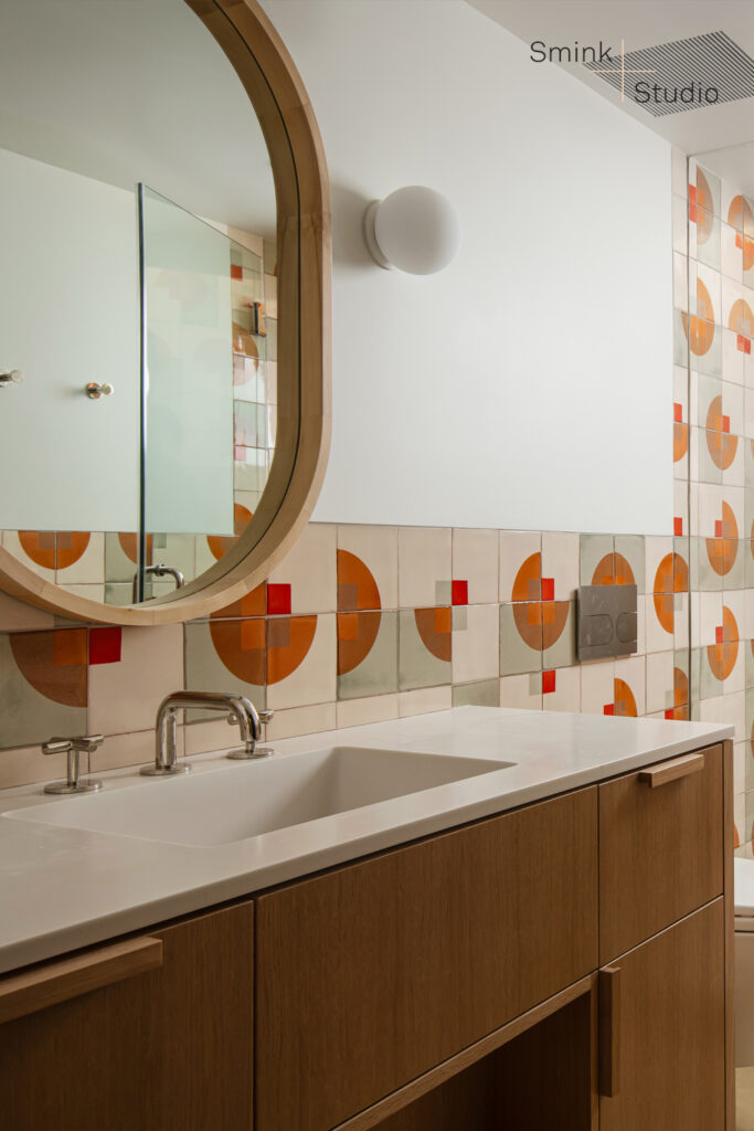Bathroom vanity with an oval mirror and a wall of Smink Studio screen-printed tiles in burnt orange, rust and red half-circles.