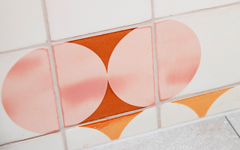 Close-up of Smink Studio glazed ceramic tiles with blush and orange screen-printed half-circles, showing the glossy handmade glaze.