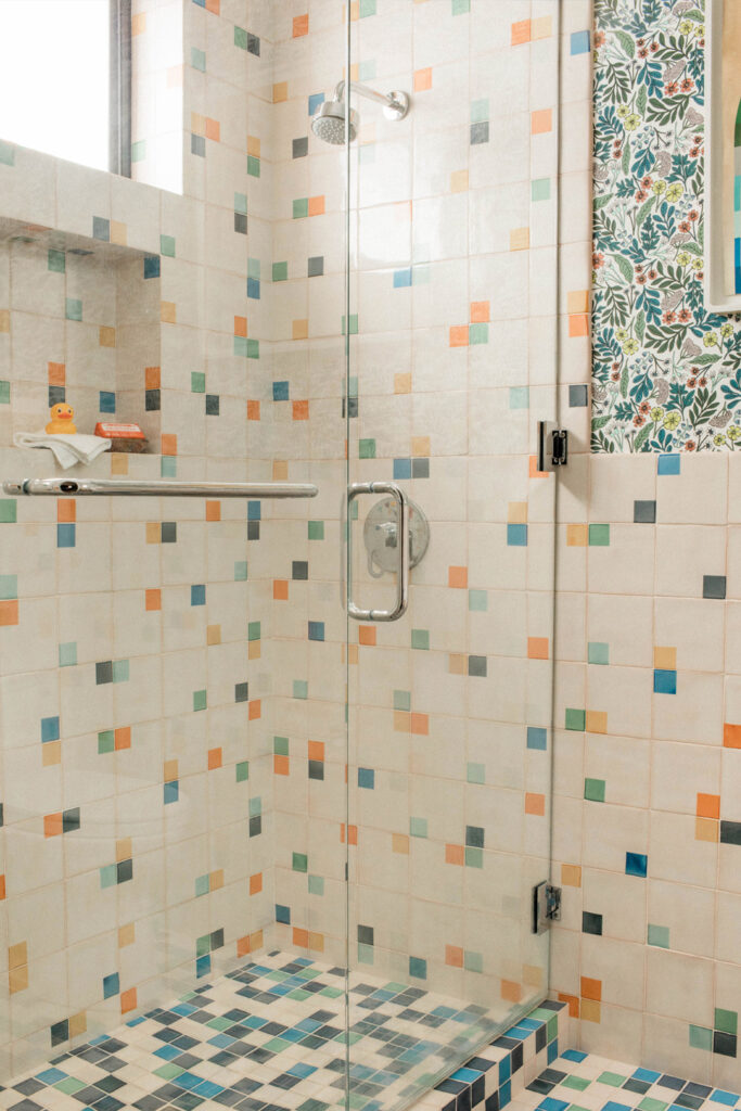 Walk-in shower of white Smink Studio handmade tiles scattered with small screen-printed squares in blue, green, orange and pink.