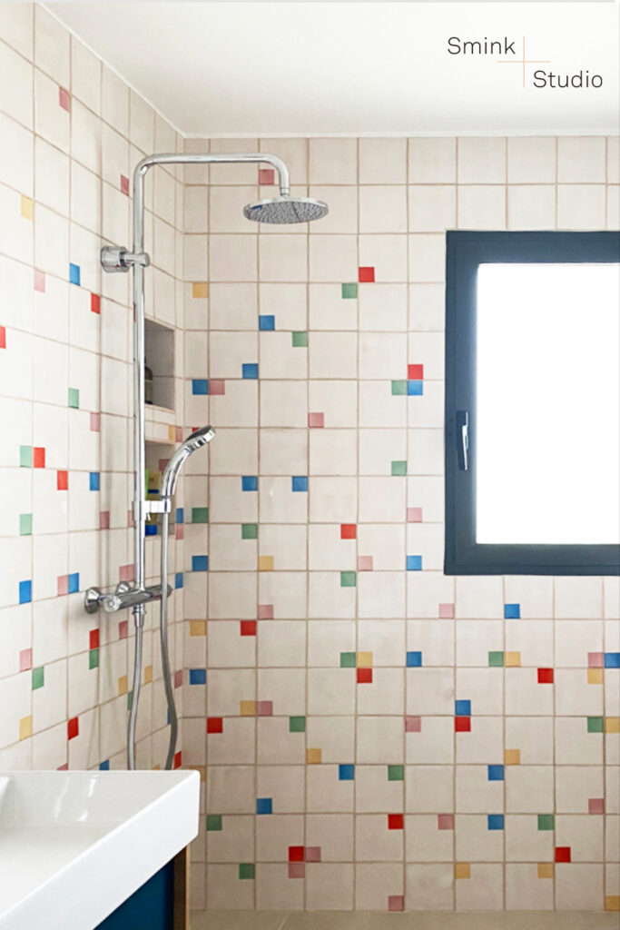 Bathroom shower of white Smink Studio glazed ceramic tiles scattered with small red, blue, yellow and green screen-printed squares.