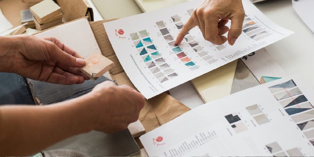 Hands pointing at colour charts and tile samples while choosing glazes for Smink Studio handmade tiles.