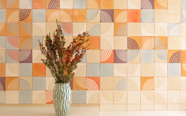 Vase of dried flowers before a splashback of Smink Studio screen-printed tiles in peach, orange, lilac and blue arcs.