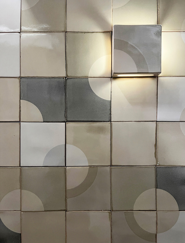 Wall of grey and white Smink Studio handmade tiles with subtle screen-printed circles, lit by a square wall light.