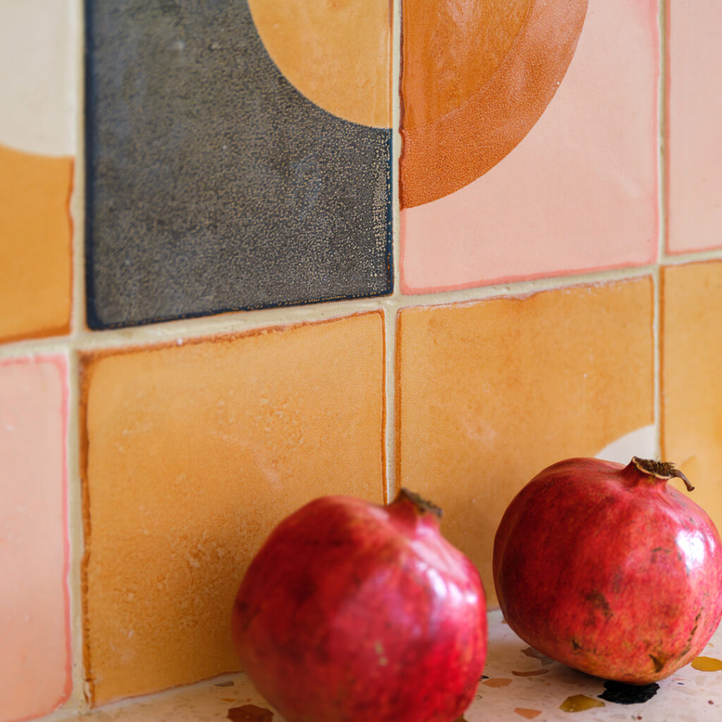 Pomegranates against a splashback of Smink Studio glazed ceramic tiles in mustard, blush and charcoal with a screen-printed orange half-circle.