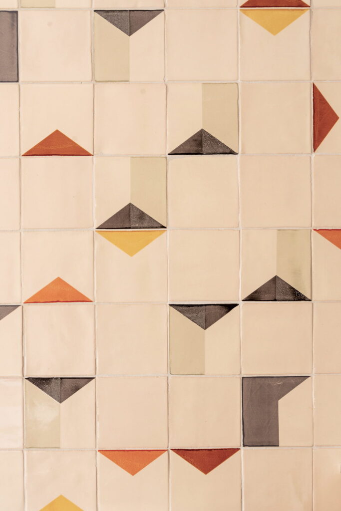 Close-up of Smink Studio handmade ceramic tiles in cream with scattered orange, mustard, red and charcoal triangle motifs in screen-printed colours.