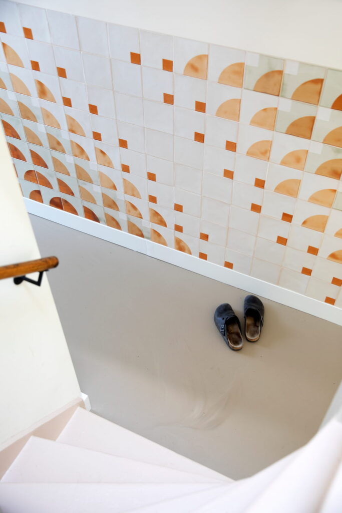 Stairwell with a half-height wall of Smink Studio handmade ceramic tiles in white, orange and sage-green half-circle screen-printed colours.