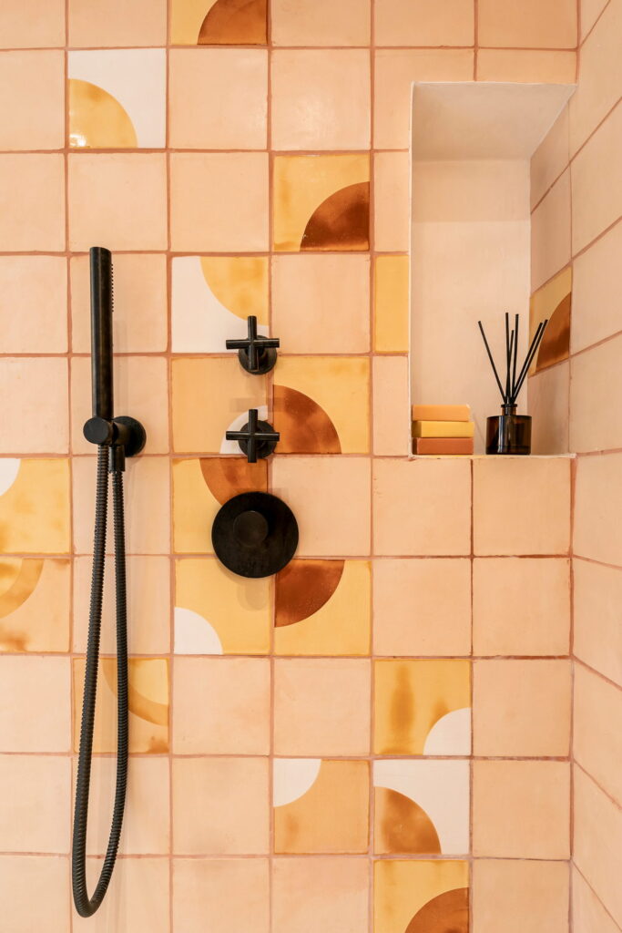 Shower of peach and terracotta Smink Studio handmade ceramic tiles with mustard and rust half-circle screen-printed colours, black fittings and a tiled niche.