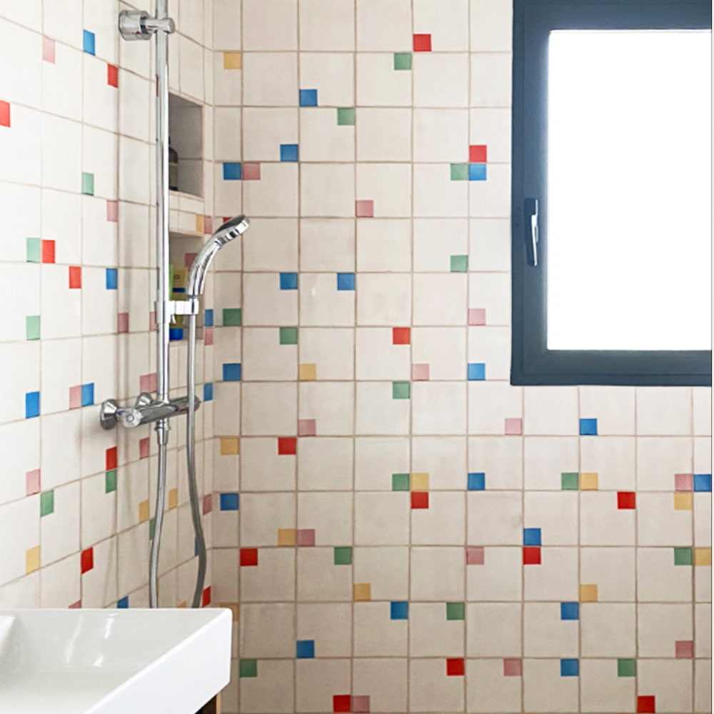 Shower of cream Smink Studio handmade ceramic tiles scattered with red, blue, green and yellow square accents in screen-printed colours, with a chrome shower.