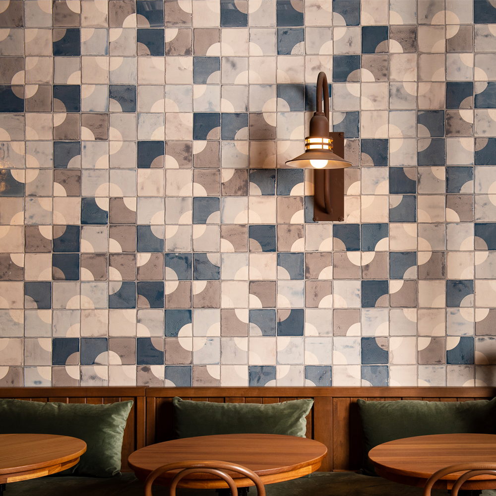 Restaurant wall of Smink Studio handmade ceramic tiles in navy, grey, taupe and cream half-circle screen-printed colours, with a wall lantern and green banquette.