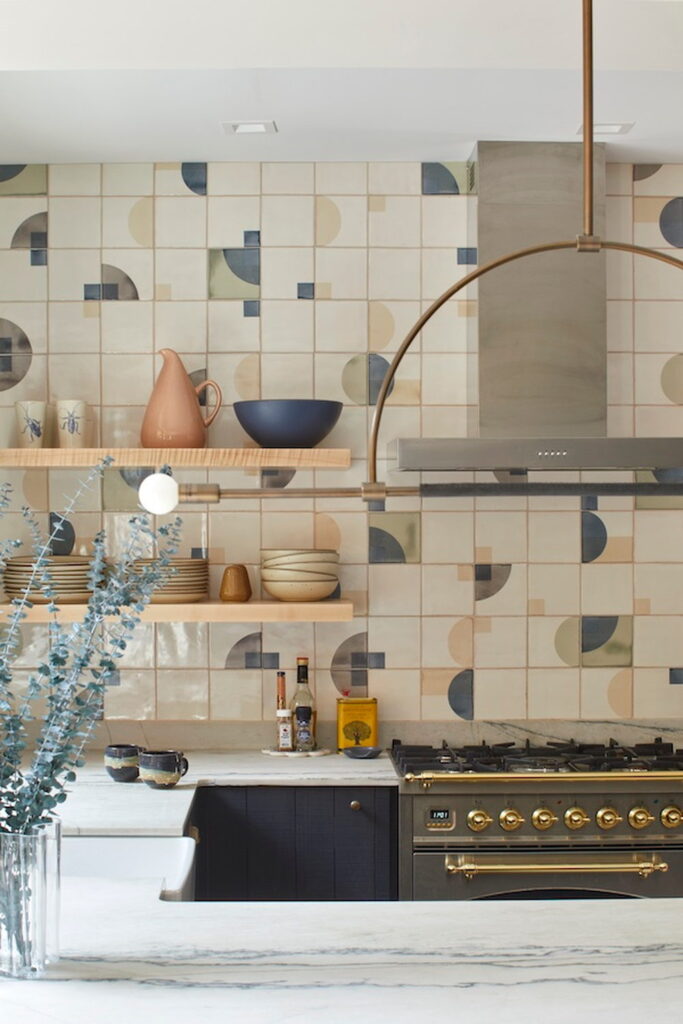 Kitchen backed by Smink Studio handmade ceramic tiles in cream with sage-green, navy and taupe half-circle screen-printed colours, with floating shelves and a black range.