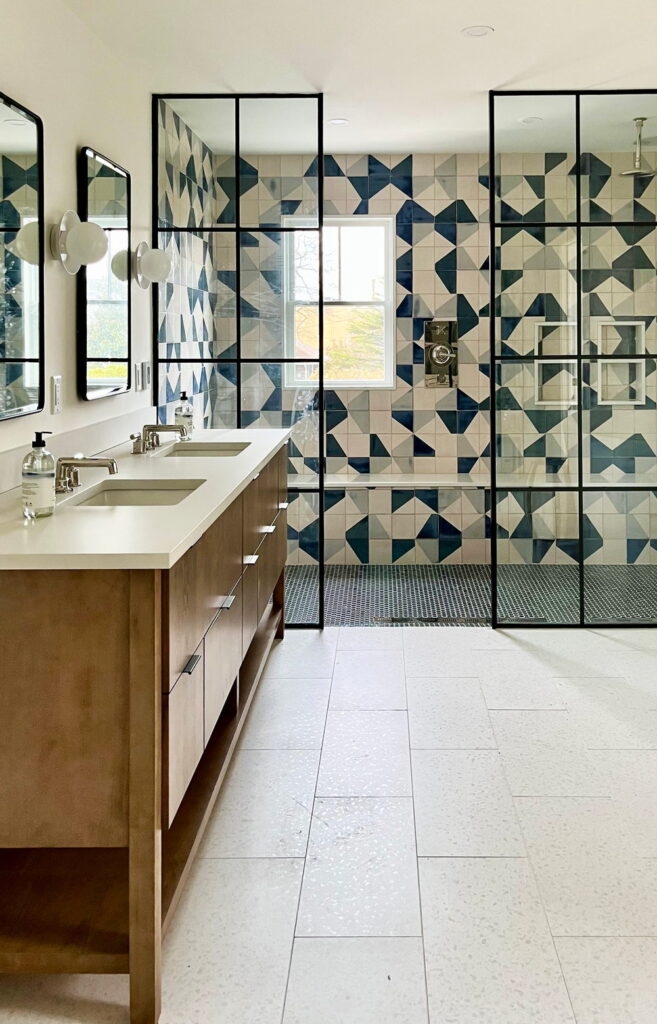 Bathroom of blue, navy and cream Smink Studio handmade ceramic tiles with bold geometric screen-printed colours, in a walk-in shower with black-framed glass screens.