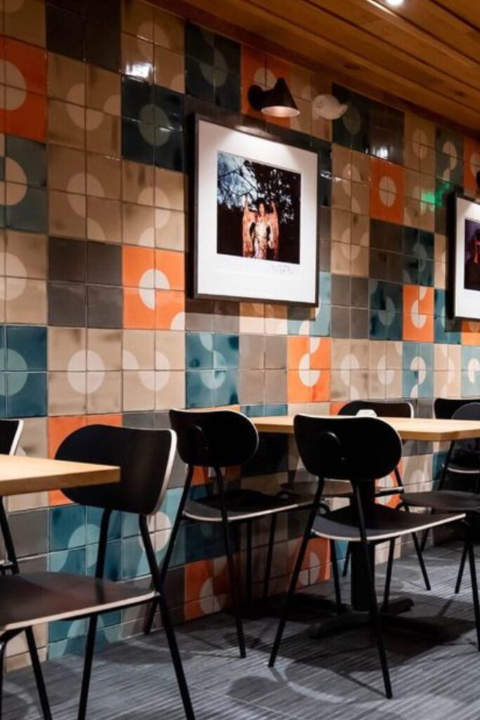 Restaurant wall of Smink Studio handmade ceramic tiles in orange, teal, grey and cream circle screen-printed colours, with framed artwork above wood tables.