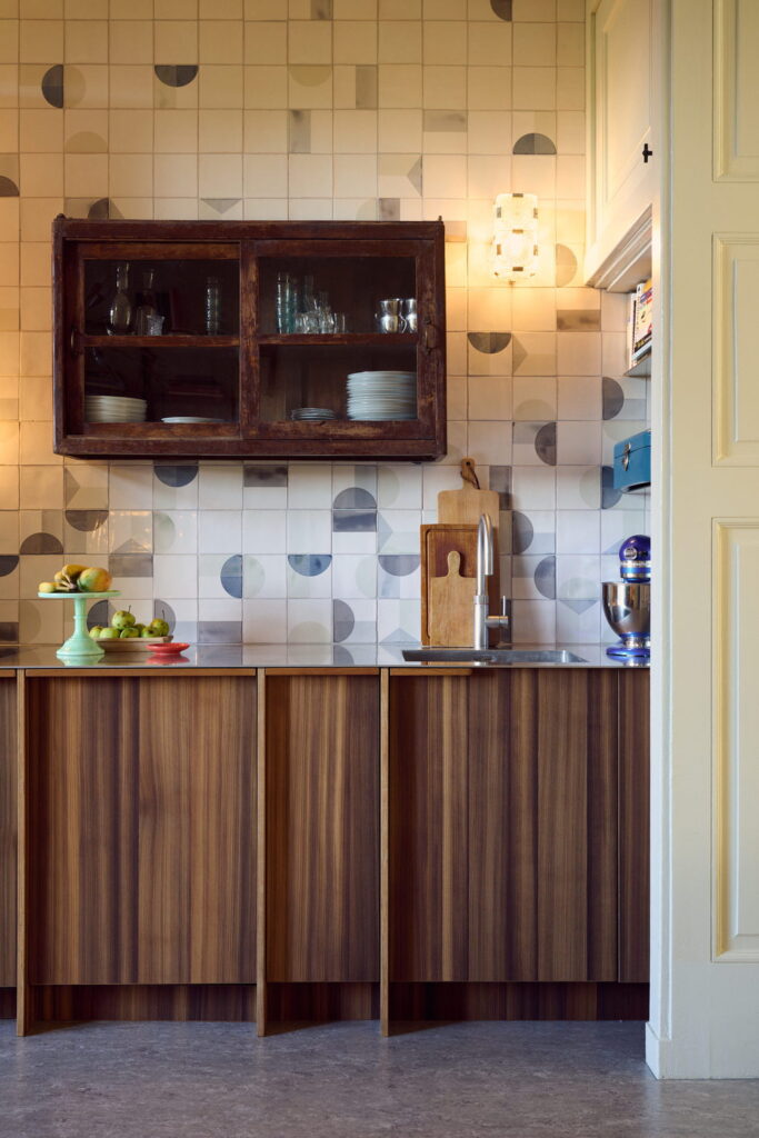 Kitchen backed by Smink Studio handmade ceramic tiles in white with grey and navy half-circle screen-printed colours, with a vintage glass cabinet and walnut units.