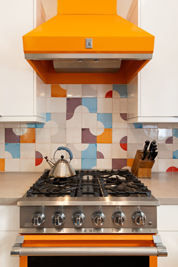 Kitchen of Smink Studio handmade ceramic tiles in cream, blue, purple, orange and red half-circle screen-printed colours, behind an orange range hood and cooker.