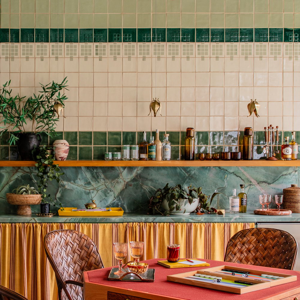 Bar area of Smink Studio handmade ceramic tiles in cream and green with a grid-motif border in screen-printed colours, with a green marble shelf and brass hooks.