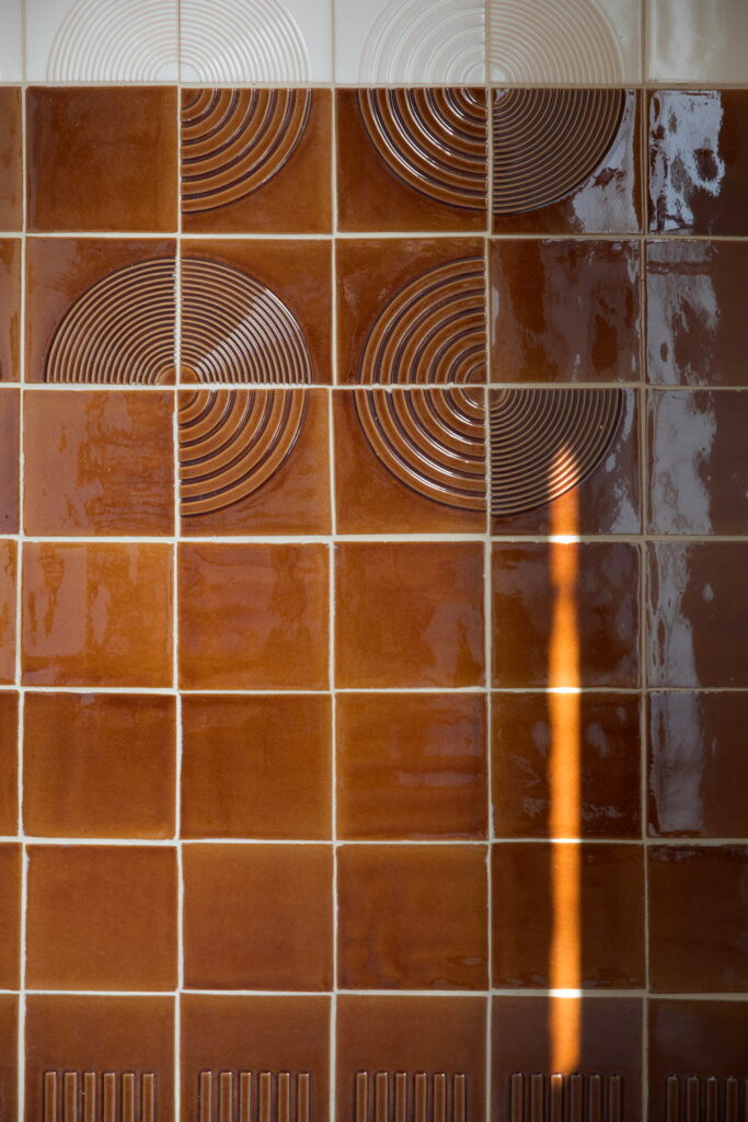 Detail of glossy caramel-brown Smink Studio handmade ceramic tiles with a raised concentric-circle relief pattern and fluted base tiles.