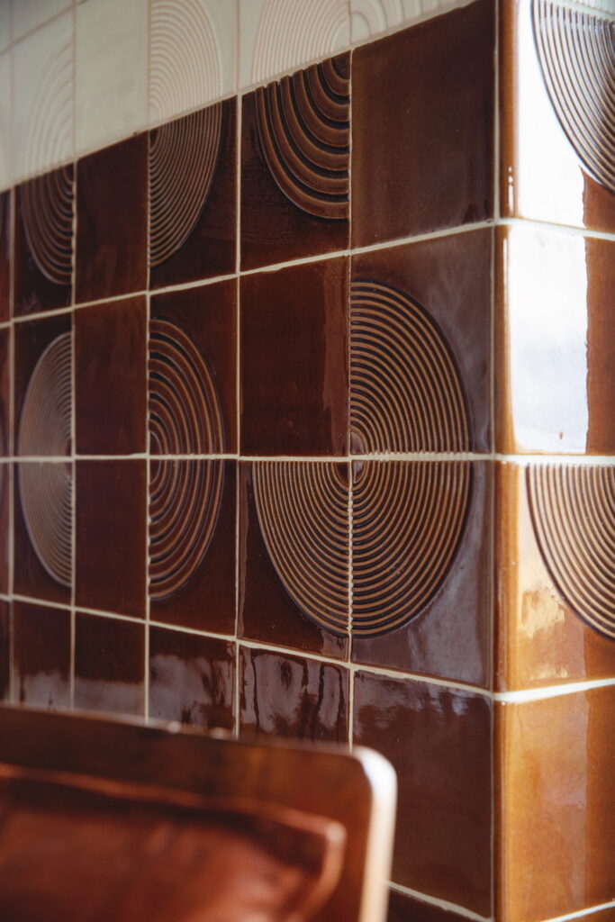 Angled detail of glossy caramel Smink Studio handmade ceramic tiles with a raised concentric-circle relief pattern.