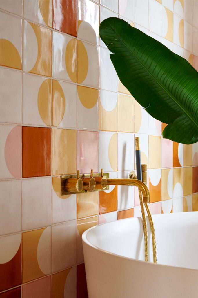 Bathroom of Smink Studio handmade ceramic tiles in white, orange, yellow, pink and terracotta half-circle screen-printed colours, with a freestanding bath and brass filler.