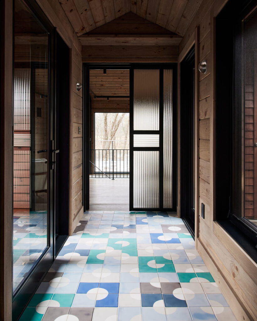 Timber-clad hallway with a floor of Smink Studio handmade ceramic tiles in blue, teal, grey and cream circle screen-printed colours, and a fluted glass door.
