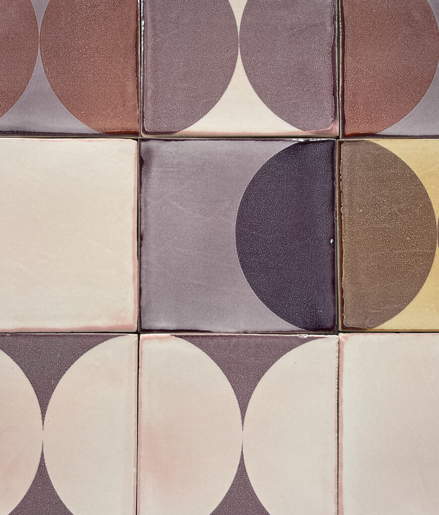 Detail of Smink Studio glazed ceramic tiles with screen-printed half-circles in aubergine, mauve and cream, showing the variation of handmade glazes.