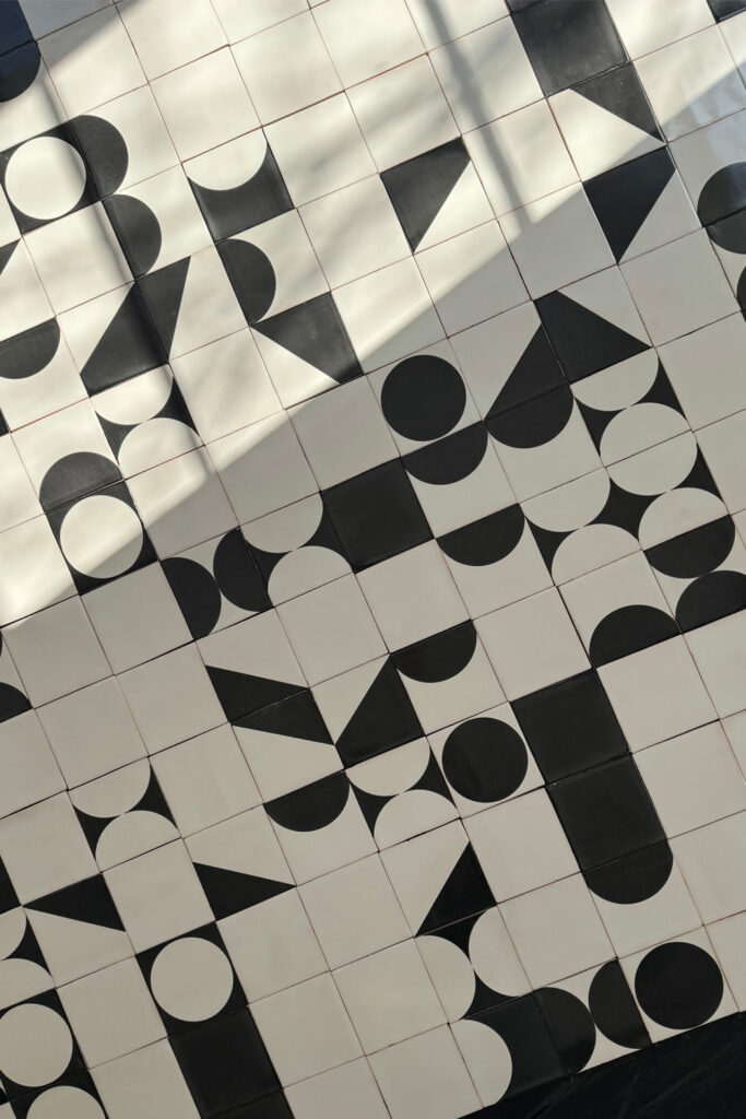 Close-up of white glazed ceramic tiles with bold black screen-printed geometric shapes, a Smink Studio wall for Imraum Design.