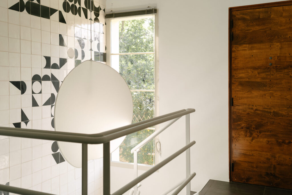 Landing with a steel balustrade, paper pendant and wooden door, set against black and white Smink Studio screen-printed ceramic tiles.