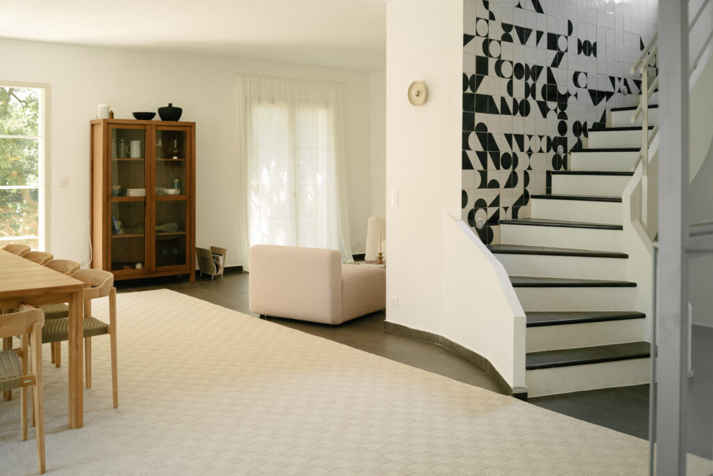 Living room with a white staircase beside a wall of black and white Smink Studio screen-printed tiles, in an interior by Imraum Design.