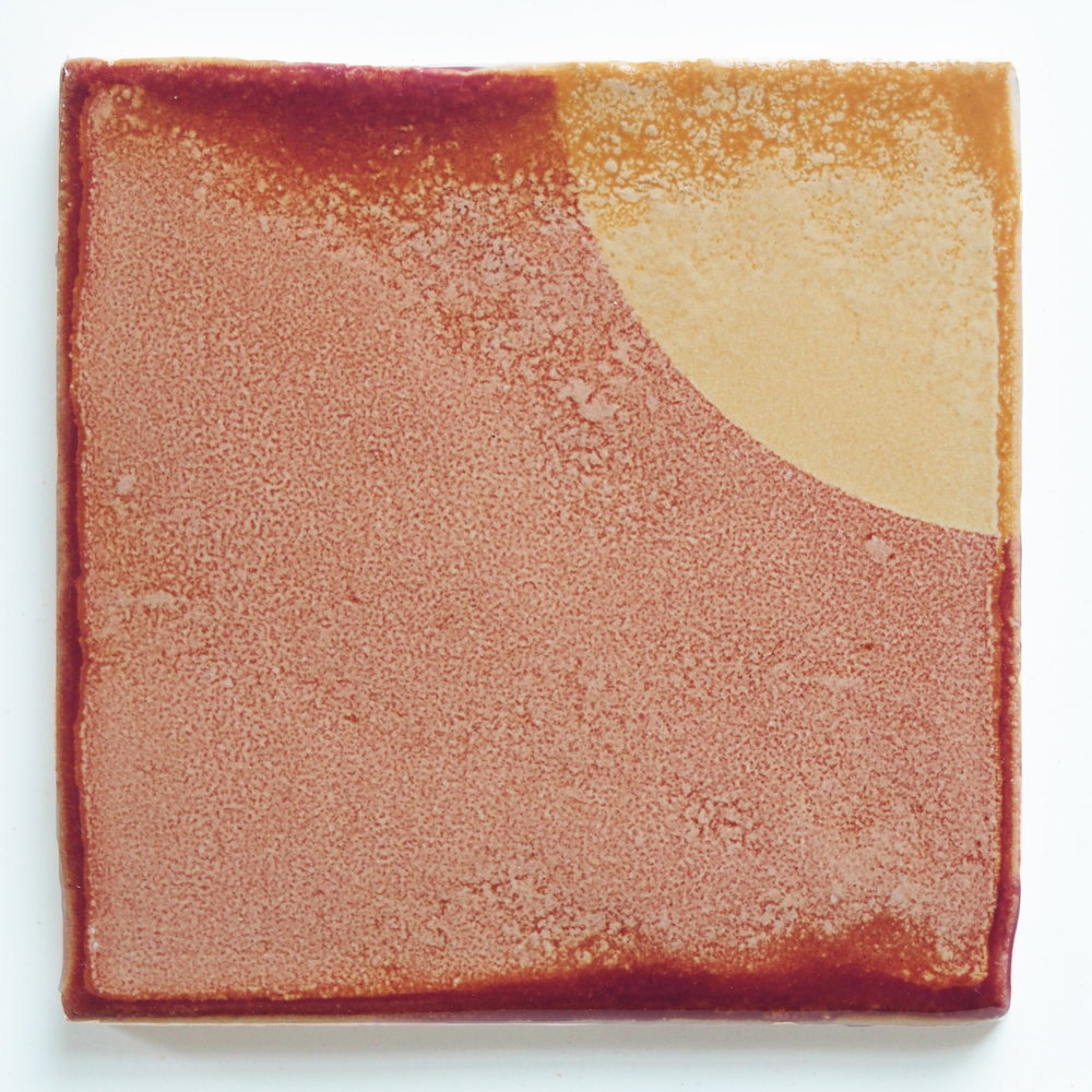 Close-up of a single handmade Smink Studio tile with raised edges, the surface mottled rust and pink with a pale yellow quarter-circle in one corner.