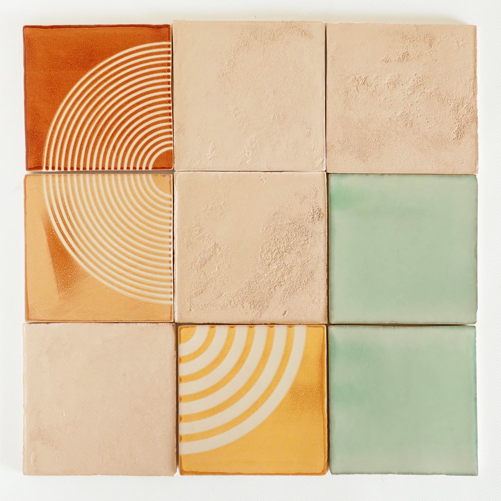 Nine Smink Studio tiles arranged in a grid, mixing Ley lines tiles with raised concentric arcs in amber and orange, plain sage green tiles, and tiles turned to show the unglazed clay back.