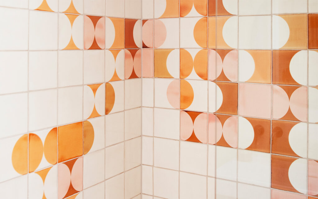 Corner of a wall in white Smink Studio tiles with screen-printed half-circles in orange, peach and blush pink.