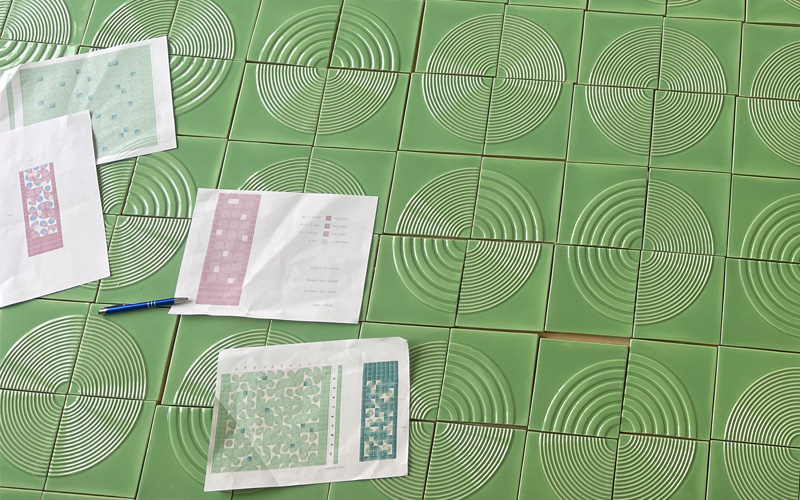 Green handmade Relief tiles on the floor with print outs of the layout design