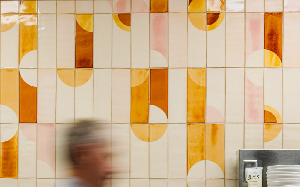 Vertical Smink Studio handmade tiles with amber, orange and pink half-circles on a wall at Próximo restaurant, North Carolina.