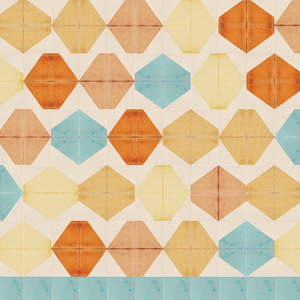 Smink Studio handmade tiles screen-printed with large hexagons in orange, terracotta, yellow and pale blue across cream, from the Is it a spencer? design.